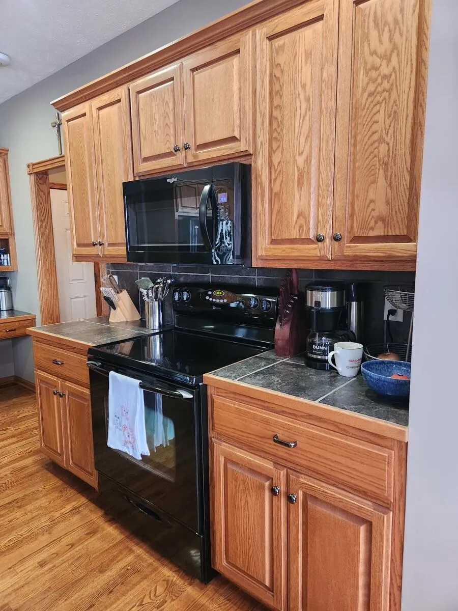 Black electric range and over-range microwave cleaned, oak cabinets and dark tile backsplash