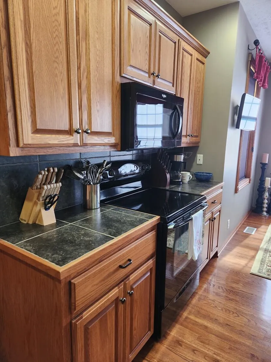 Tile countertop, knife block, and black range detailed, hardwood floor swept