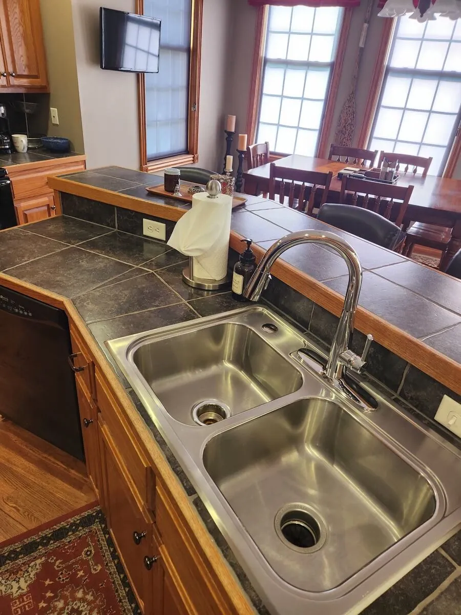Stainless double sink and dark tile peninsula wiped clean, with the dining table beyond